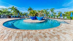 A swimming pool with lounge chairs and umbrellas, surrounded by palm trees. - Putterly Perfect 3rd Floor Golf Front Condo (Bradenton)