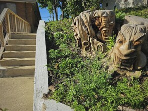 Una escalera conduce a un edificio con un muro de concreto y un área verde con una gran escultura de madera.