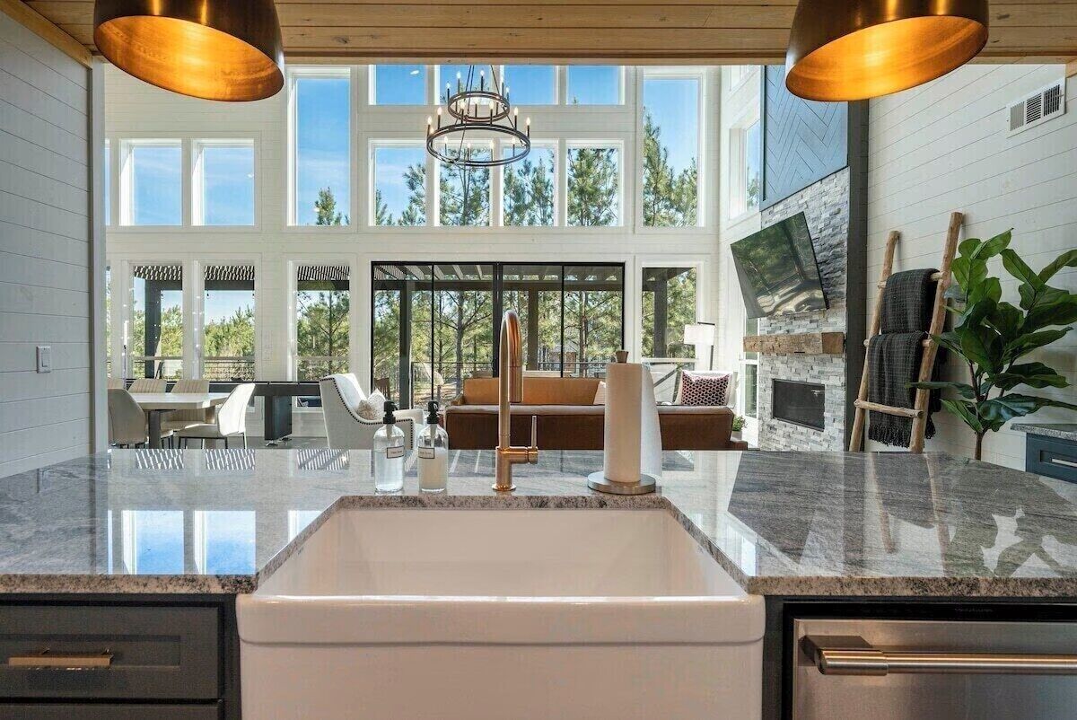 A modern kitchen with a large island, a chandelier, and a view of the outdoors.