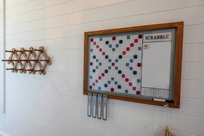 A Scrabble board game set up on a wall with a wooden rack and letter tiles below it. - NEW! Pondside Lux Cabin with Hot Tub, King Suites, Fire Pit & Game Loft (Broken Bow)