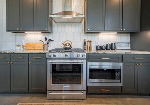 A kitchen with dark cabinets, a gas stove, an oven, and a microwave. - NEW! Pondside Lux Cabin with Hot Tub, King Suites, Fire Pit & Game Loft (Broken Bow)