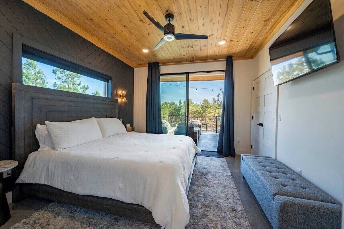 A bedroom with a large bed, a ceiling fan, and a view of the outdoors.