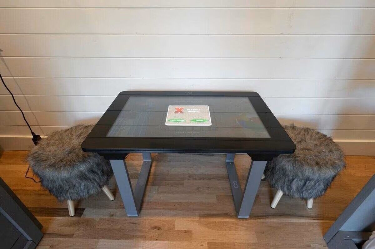 Une petite table carrée avec un plateau en verre et des pieds en métal, flanquée de deux tabourets recouverts de fourrure.