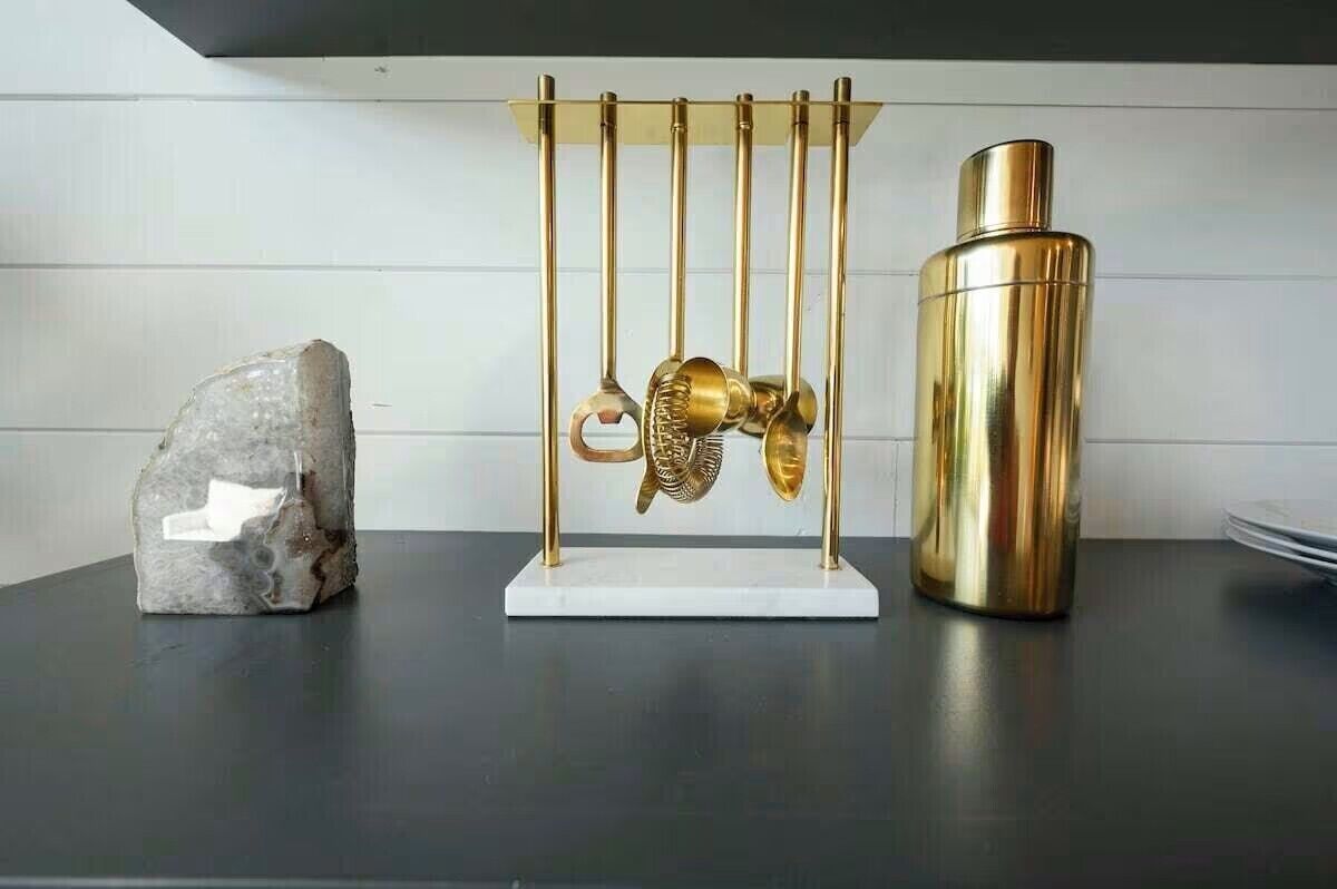 Eine Küchenarbeitsplatte mit einem dekorativen Metallregal, das Küchenutensilien, einen goldfarbenen Thermosbehälter und einen Stein beherbergt.