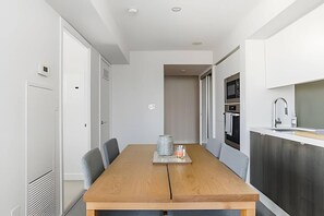 A modern kitchen with a wooden dining table, chairs, and a built-in oven. - King West Place (Toronto)