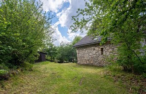Ein Gebäude aus Stein mit Ziegeldach, umgeben von üppiger Vegetation und Bäumen.