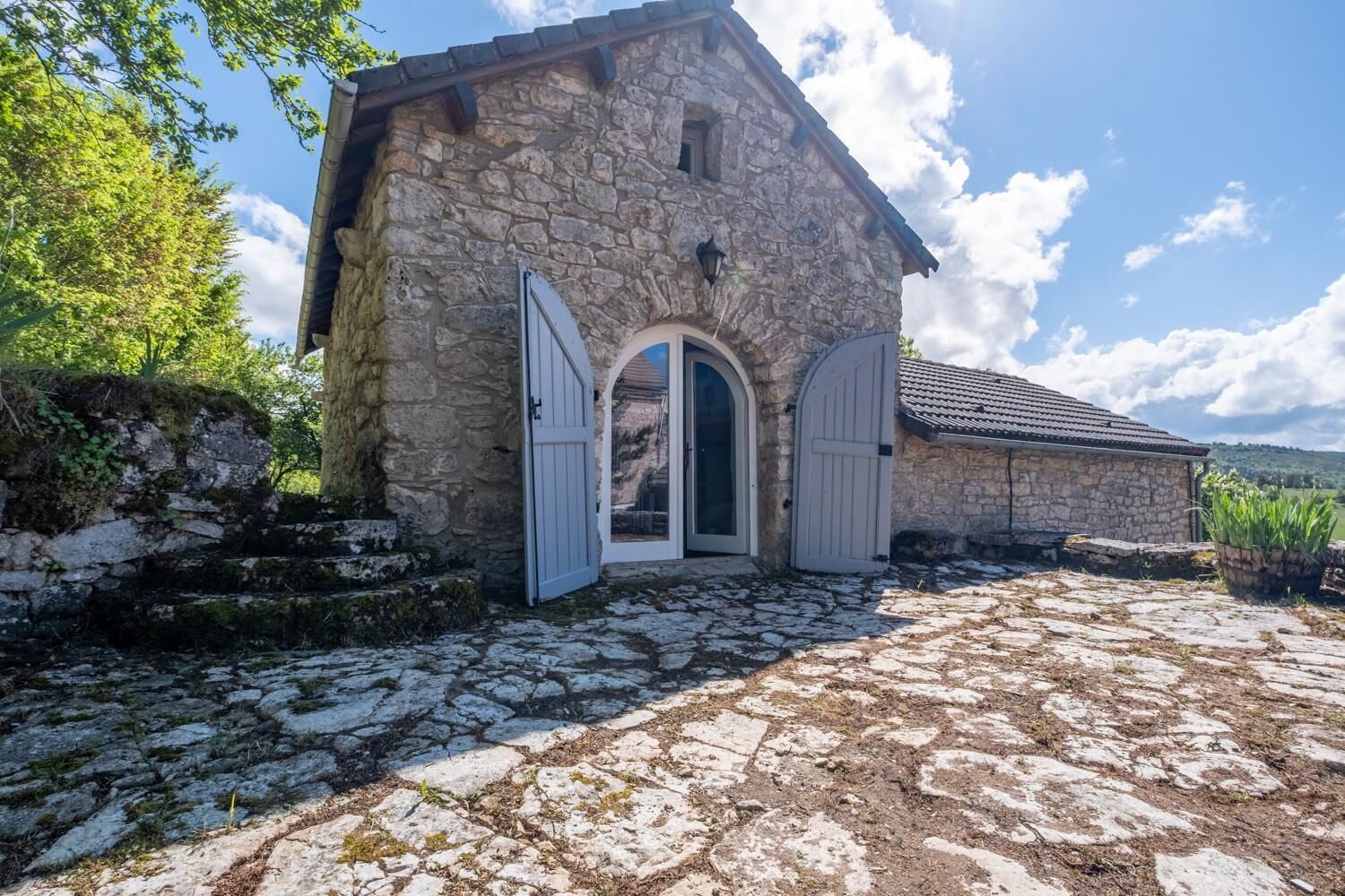 Ein Steinhaus mit zwei weißen Türen, einer Steintreppe und einem gepflasterten Innenhof.