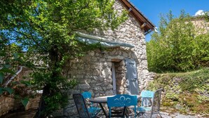 A stone building with a rustic exterior, a small door, and a table with chairs outside. - Le Barrinal - MAS-SAINT-CHELY (MAS-SAINT-CHELY)