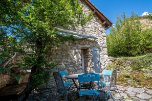 Ein Steinhaus mit rustikaler Fassade, einer kleinen Tür und einem Tisch mit Stühlen vor der Tür.