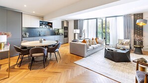 Una cocina moderna con comedor, una sala de estar con sofá y mesa de centro, y ventanas amplias con cortinas.
