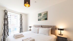 Ein Hotelzimmer mit einem großen Bett, zwei Nachttischen, einem Bild an der Wand und einem Fenster mit Vorhängen.