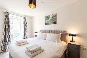 Ein Hotelzimmer mit einem großen Bett, zwei Nachttischen, einem Bild an der Wand und einem Fenster mit Vorhängen.
