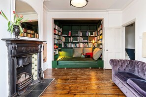 Ein Zimmer mit Kamin, einem grünen Sofa, einem violetten Sofa und einem Bücherregal voller Bücher.