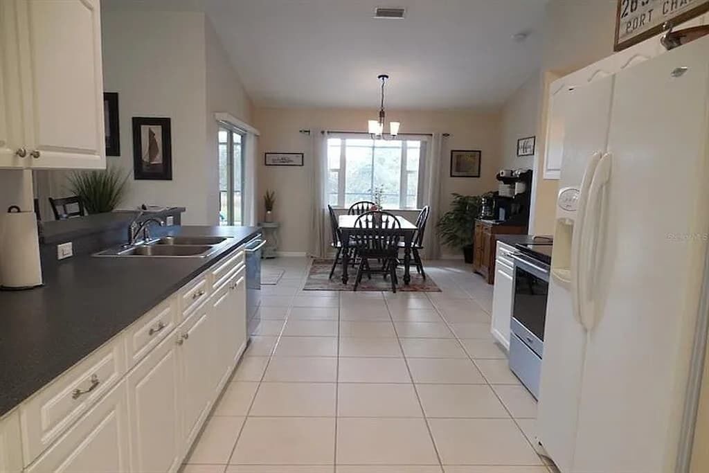 Una cocina con comedor, armarios blancos, un refrigerador y un ventanal.