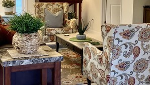 Un salon comprenant un canapé, un fauteuil, une table basse et une lampe. Il y a une porte et un tableau encadré au mur.