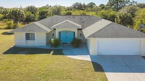 Une maison de plain-pied avec un garage à l’avant, une porte bleue et un petit jardin devant.