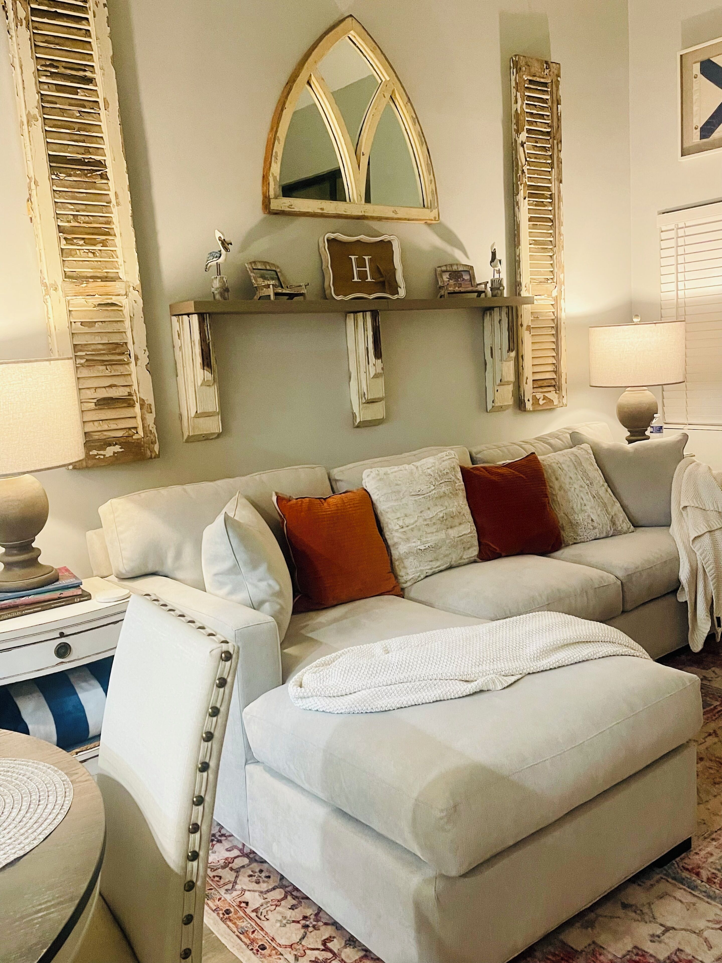 Una sala de estar con un sofá blanco, un espejo decorativo y una estantería con diversos objetos.