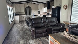 A spacious living room with a leather sofa, wooden coffee table, and a kitchen in the background.