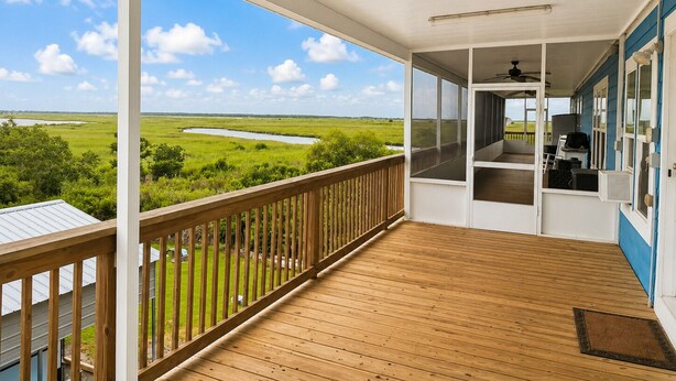A covered porch with a view of a green landscape and a body of water.