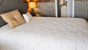 A bedroom with a large bed, wooden walls, a mirror, and a nightstand with a lamp.