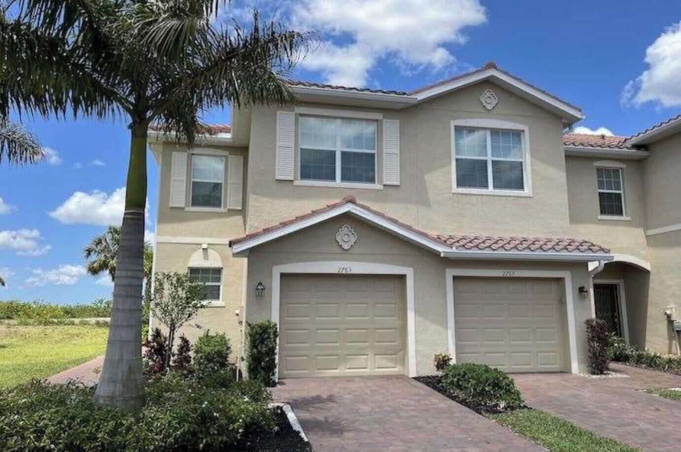 A two-story house with a garage, a driveway, and a palm tree.