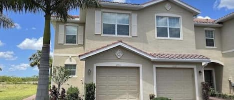A two-story house with a garage, a driveway, and a palm tree.