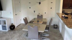 Un comedor con un reloj, sillas, una mesa y una encimera de cocina.