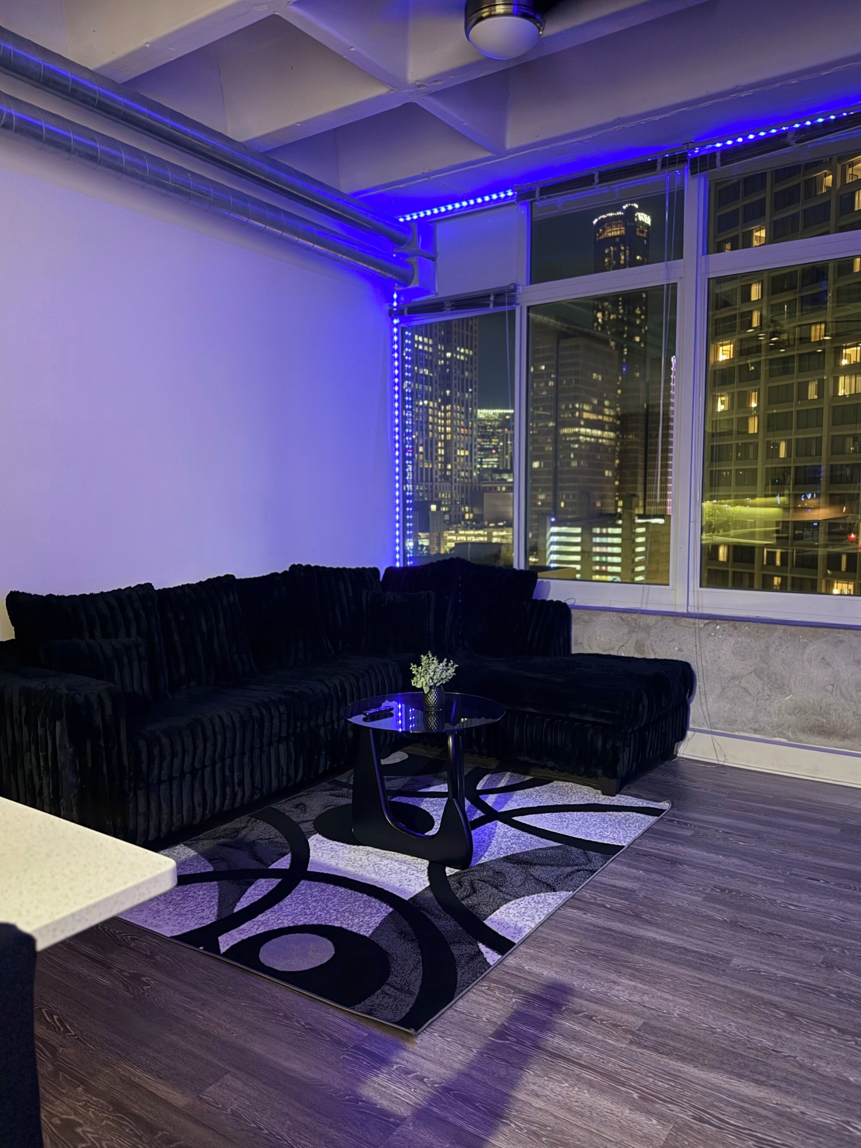 A modern living room with a black sectional sofa, a round black coffee table, and a patterned rug.
