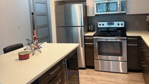 A modern kitchen with stainless steel appliances, a wooden dining table, and a pendant light. - The Midnight Luxury Condo With Pool, Gym & Minutes to Downtown ATL (Atlanta)