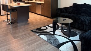 A modern kitchen with a central island, bar stools, a dining table, and a black sofa with a patterned rug. - The Midnight Luxury Condo With Pool, Gym & Minutes to Downtown ATL (Atlanta)