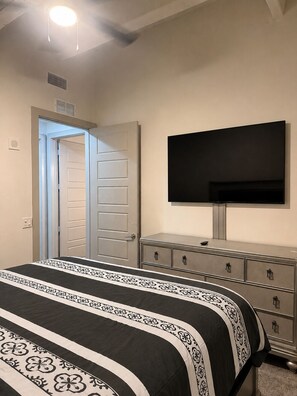 A bedroom with a bed, dresser, TV, and an open door leading to another room. - The Midnight Luxury Condo With Pool, Gym & Minutes to Downtown ATL (Atlanta)