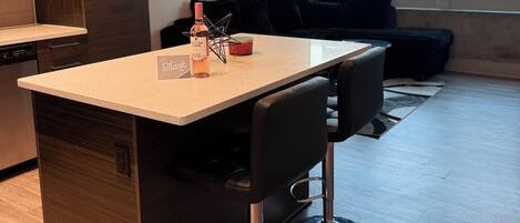 A modern kitchen with a central island, bar stools, pendant lighting, and a view of the city through large windows.