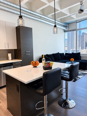 A modern kitchen with a central island, bar stools, and a view of the city through large windows. - The Midnight Luxury Condo With Pool, Gym & Minutes to Downtown ATL (Atlanta)