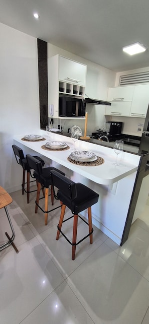 A modern kitchen with a central island, bar stools, and a dining table set for four. - Paradise between the sea and the lagoon! Premium condominium in Arraial do Cabo, Rio de Janeiro. (Arraial do Cabo)