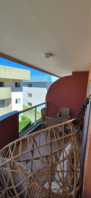 A balcony with wicker furniture, a glass table, and a view of adjacent buildings. - Paradise between the sea and the lagoon! Premium condominium in Arraial do Cabo, Rio de Janeiro. (Arraial do Cabo)