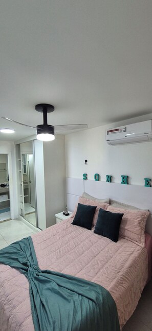 Un dormitorio con cama, ventilador de techo, aire acondicionado y espejo.