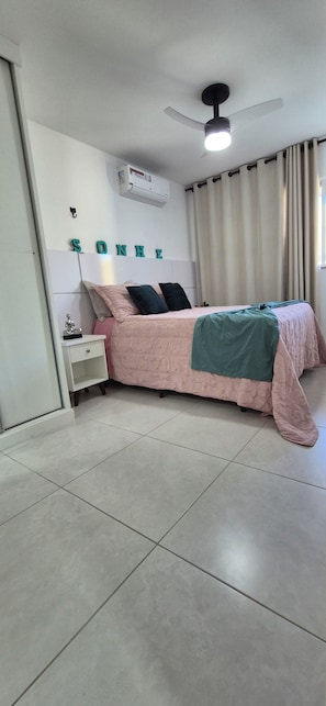 A bedroom with a bed, a bedside table, a wall-mounted air conditioner, and a ceiling fan. - Paradise between the sea and the lagoon! Premium condominium in Arraial do Cabo, Rio de Janeiro. (Arraial do Cabo)