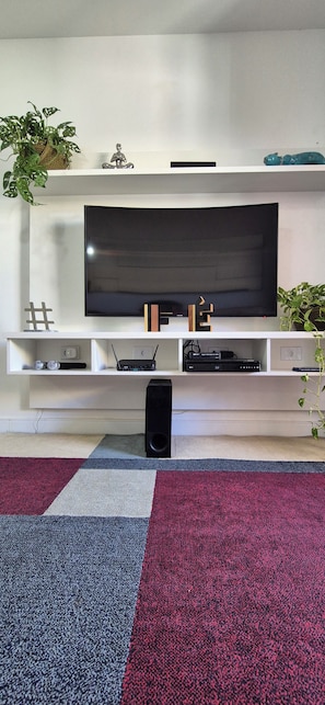 A flat-screen TV mounted on a white wall, with a black speaker in front. - Paradise between the sea and the lagoon! Premium condominium in Arraial do Cabo, Rio de Janeiro. (Arraial do Cabo)