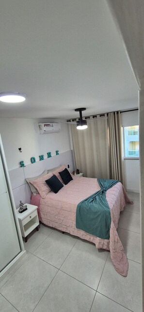 A bedroom with a bed, a nightstand, an air conditioning unit, a ceiling fan, and a window with curtains. - Paradise between the sea and the lagoon! Premium condominium in Arraial do Cabo, Rio de Janeiro. (Arraial do Cabo)