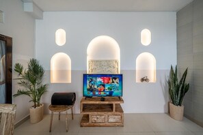 A living room with a TV on a wooden stand, three wall-mounted lights, and two potted plants. - Villa Catur Seminyak (Badung)