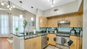 A modern kitchen with granite countertops, stainless steel appliances, wooden cabinets, and pendant lighting. - Cozy retreat minutes away from FIFA World Cup (Atlanta)