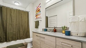 Un baño con cortina de ducha, inodoro, tocador con espejo y lavabo.