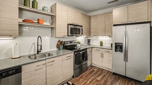 Una cocina moderna con armarios de madera clara, electrodomésticos de acero inoxidable y un tapete con estampado blanco y negro.