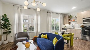 Una sala de estar moderna con sofá, sillón y mesa de comedor. Hay una zona de cocina con microondas y horno.