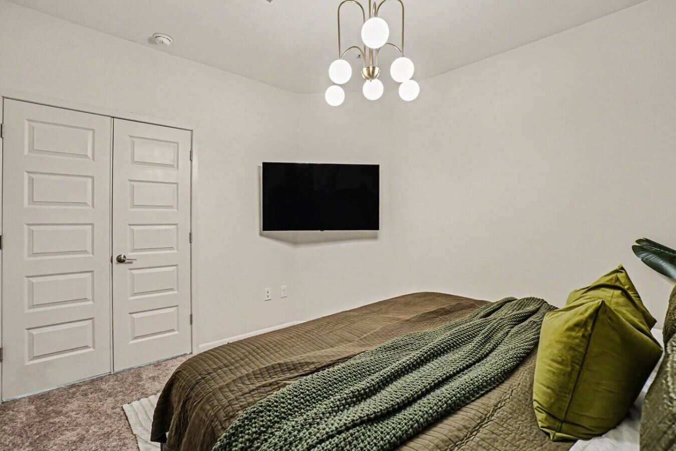 A bedroom with a bed, a TV, a white door, and a ceiling light fixture.