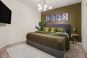 Ein Schlafzimmer mit einem Bett, einem kleinen Nachttisch, einer Lampe und einer Pflanze.