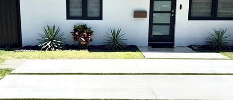 A modern two-story house with a number 8620 on the door, a front yard with grass and plants, and a clear sky.