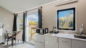 Una cocina moderna con refrigerador, microondas, hervidor de agua y ventana con vista a árboles.