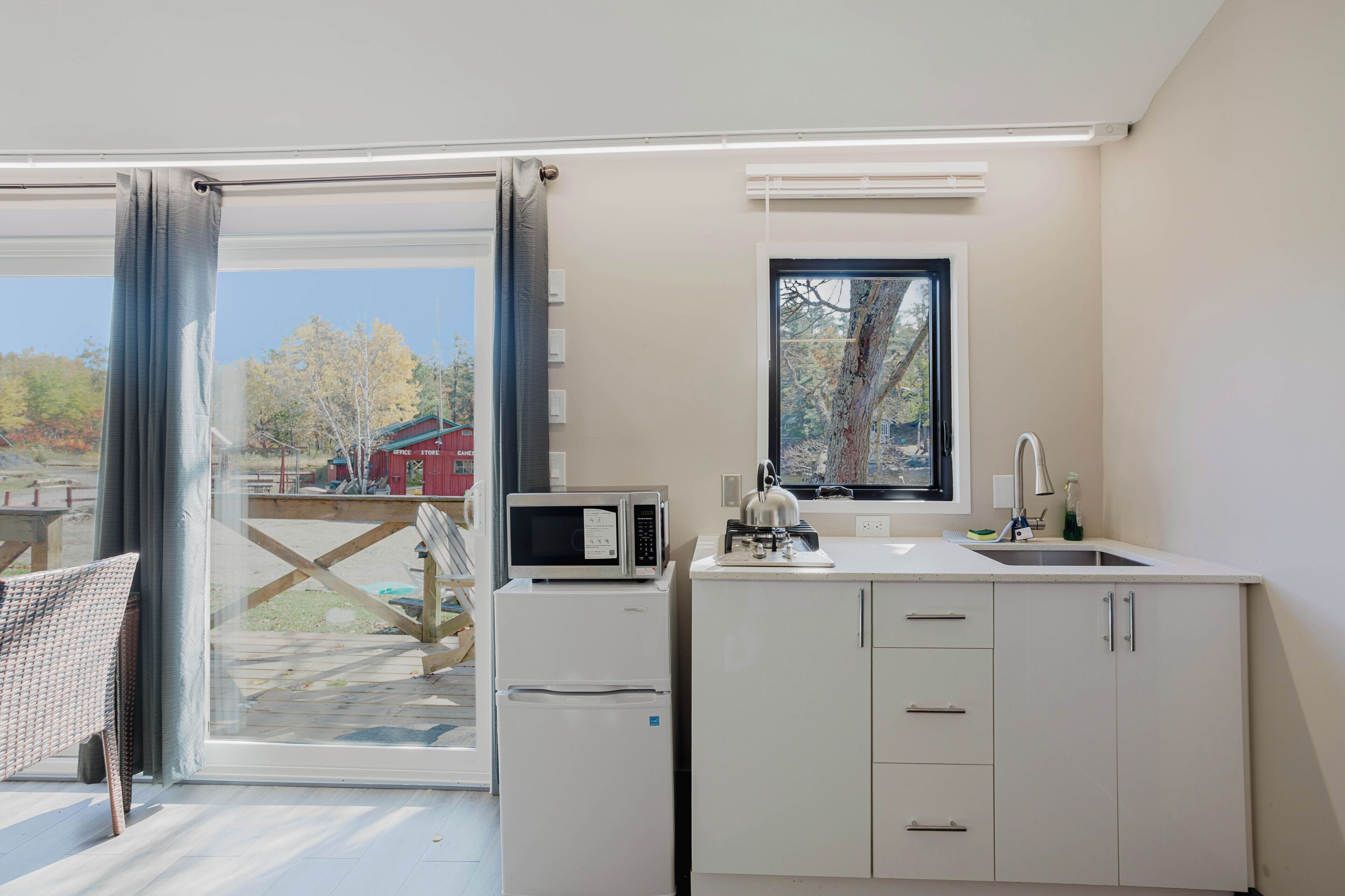 Cocina compacta con microondas, refrigerador, pileta y ventana con vista a una terraza.