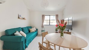 A modern living room with a teal sofa, wooden dining table, and a large window with curtains. - Located 650 meters from Tokyo Skytree, with direct access from Narita and Haneda Airports. A two-story single-family home that accommodates up to 7 guests. A 4-minute walk from the nearest station. (墨田区)